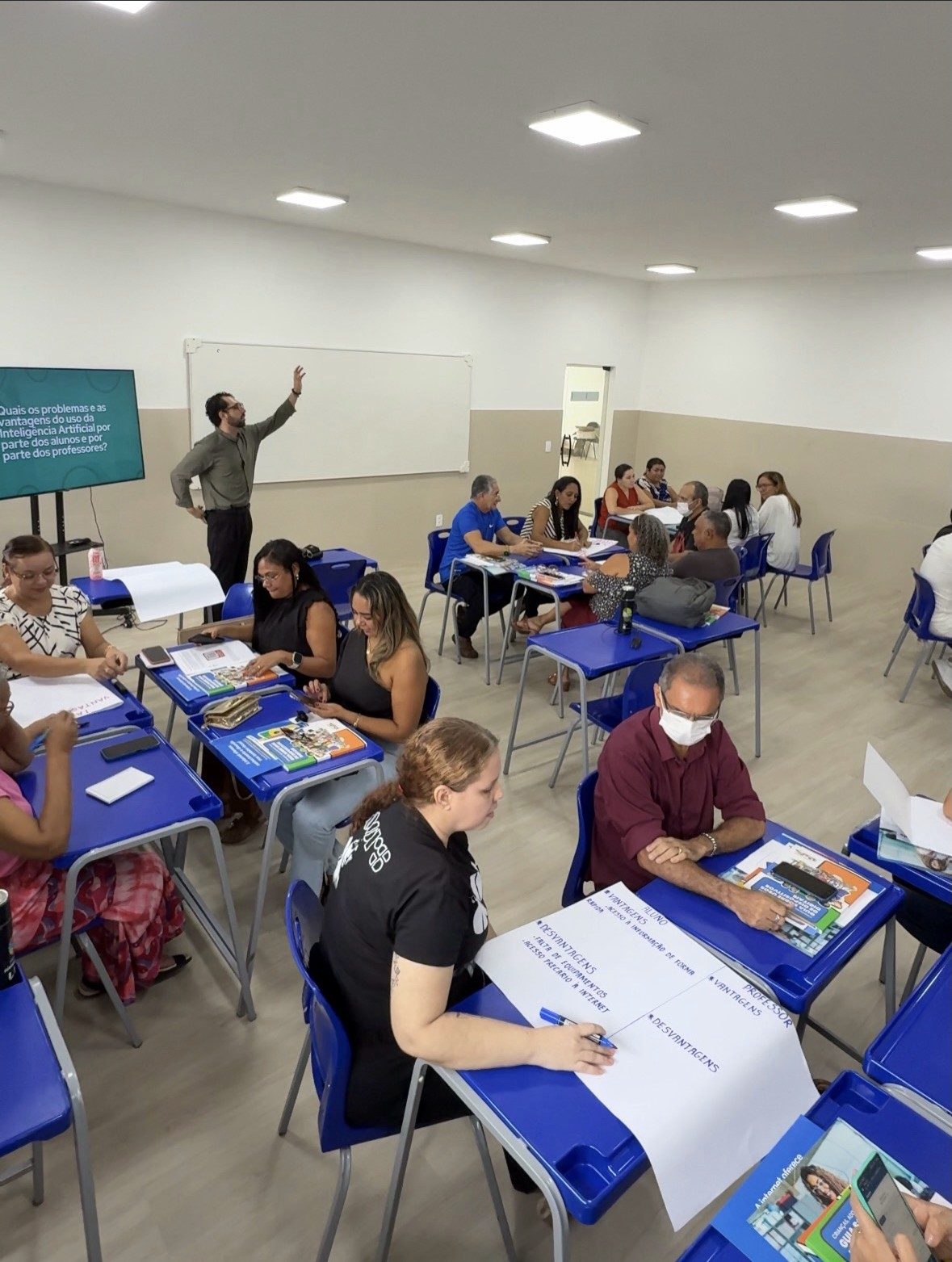 Professores trabalham em cartazes durante a oficina em Teresina, com o educador ao fundo diante da tela