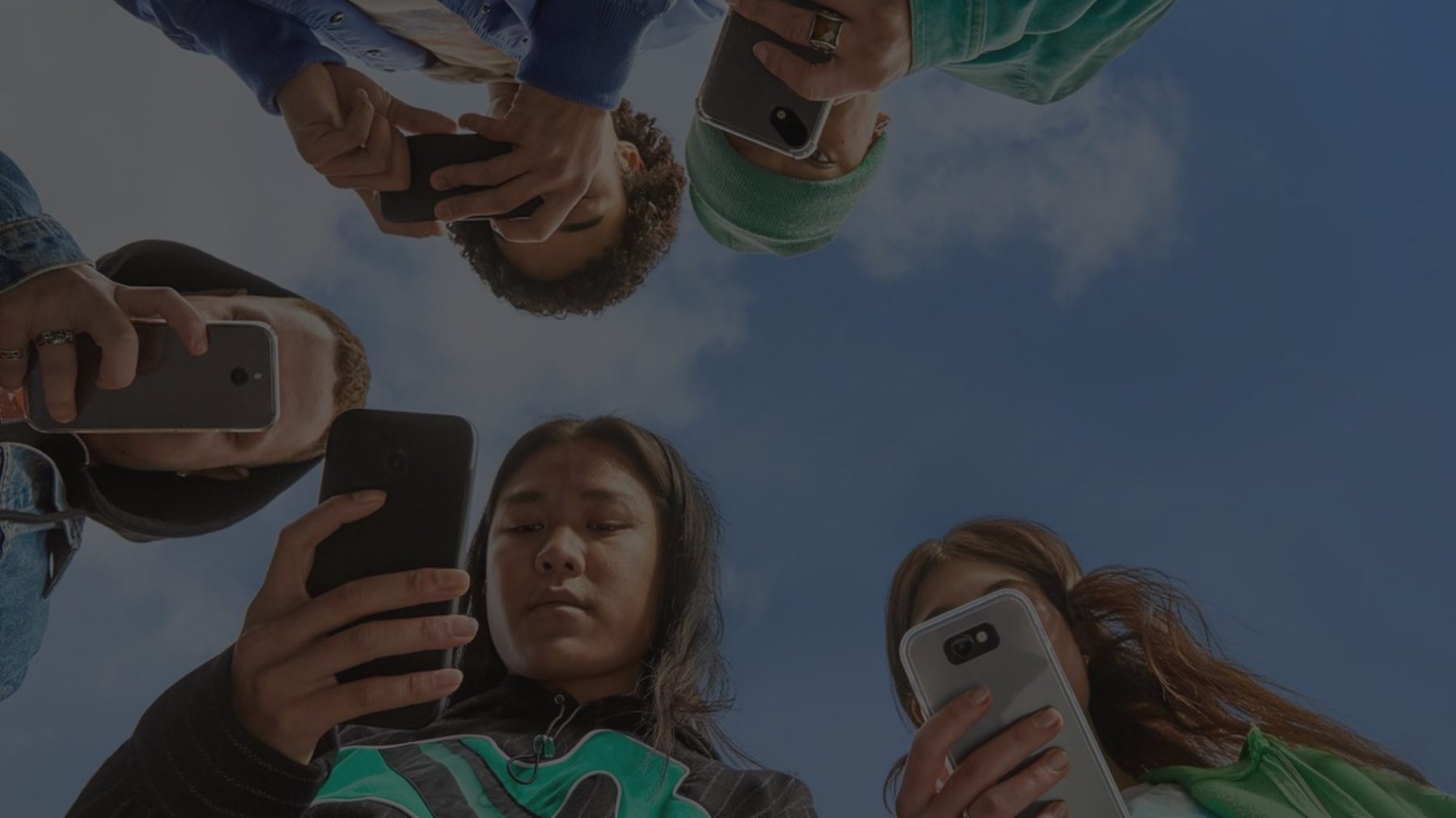 Jovens em roda, vistos de baixo, cada um olhando o próprio celular